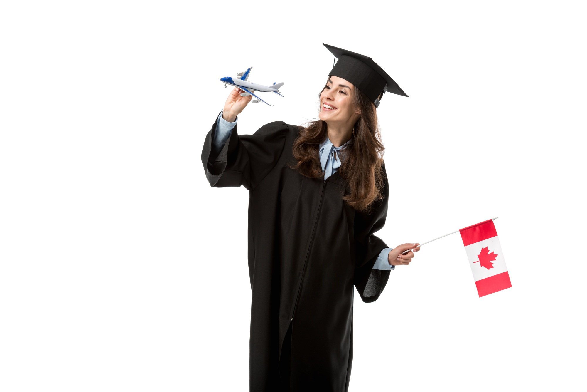 happy female student in academic gown holding canadian flag and plane model isolated on white,